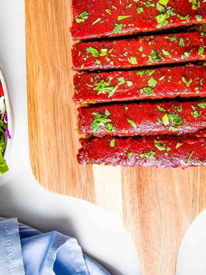 Meatloaf, with tomato sauce glaze, sprinkled with fresh herbs, cut into thick slices.