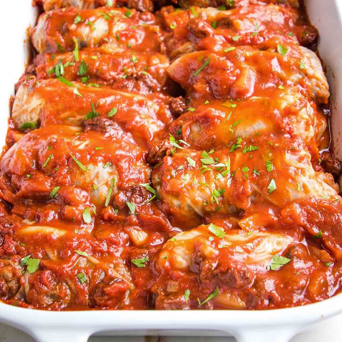 White baking dish with stuffed cabbage in red sauce with fresh herbs on top.