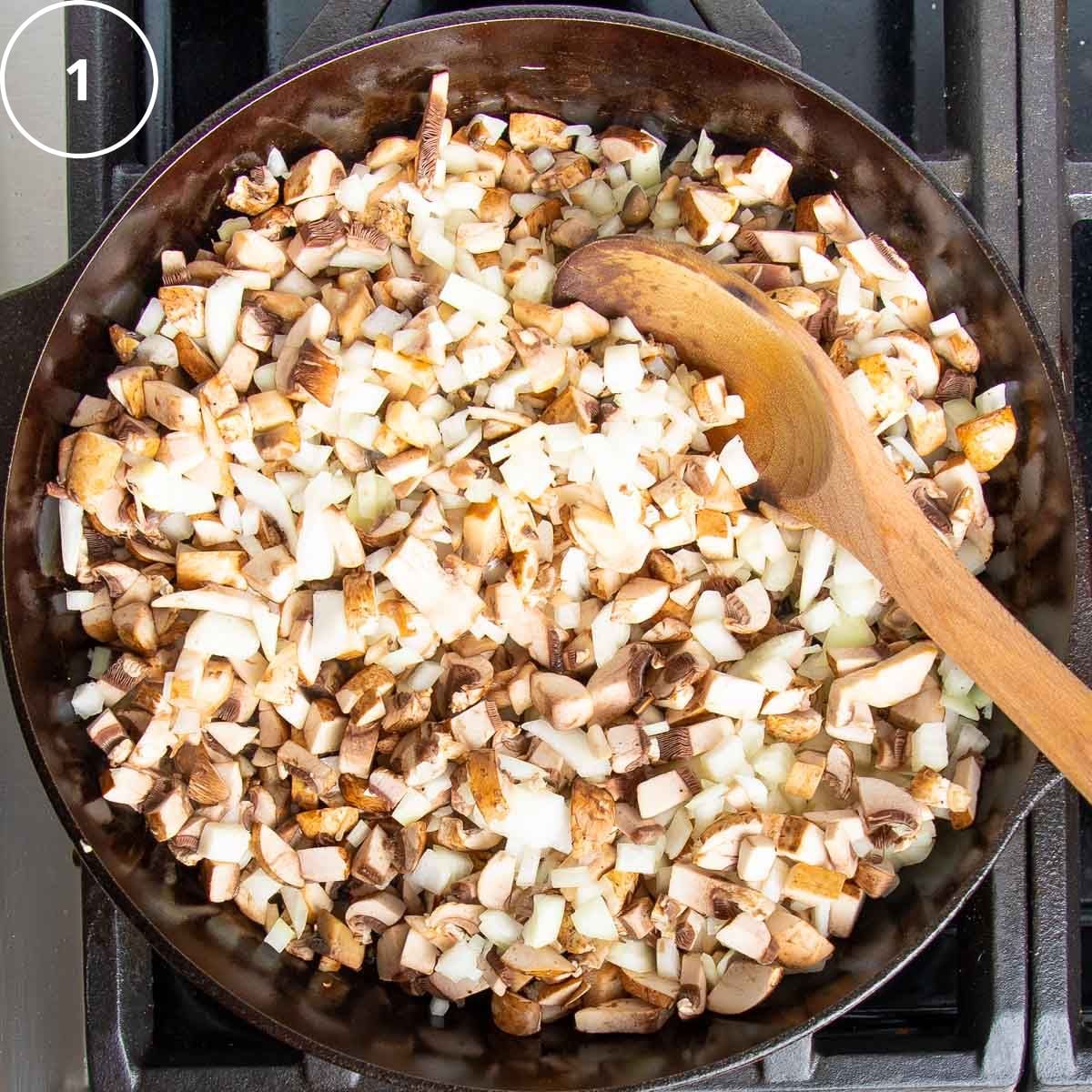 Diced onions and mushrooms in a cast iron skillet with a wooden spoon.