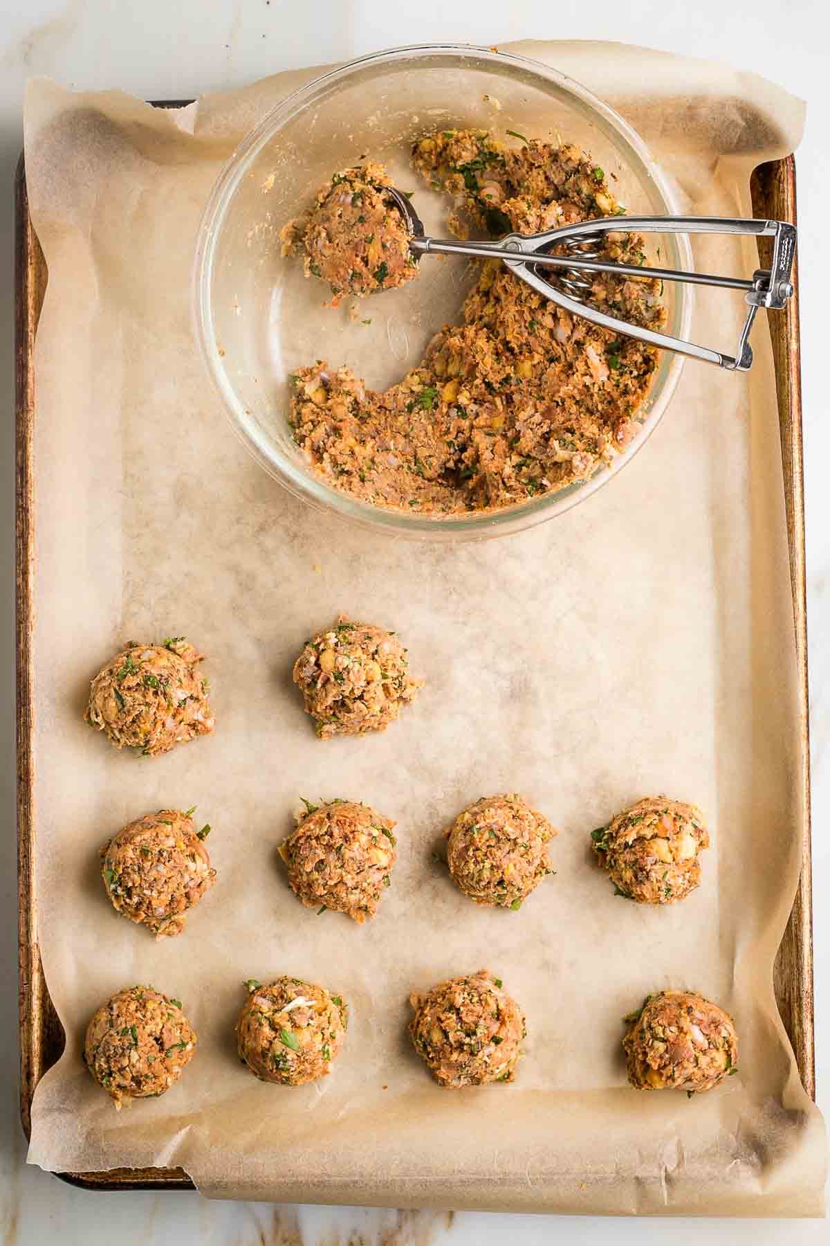 Vegan meatballs on a baking tray. Bowl with batter plus scooper too.