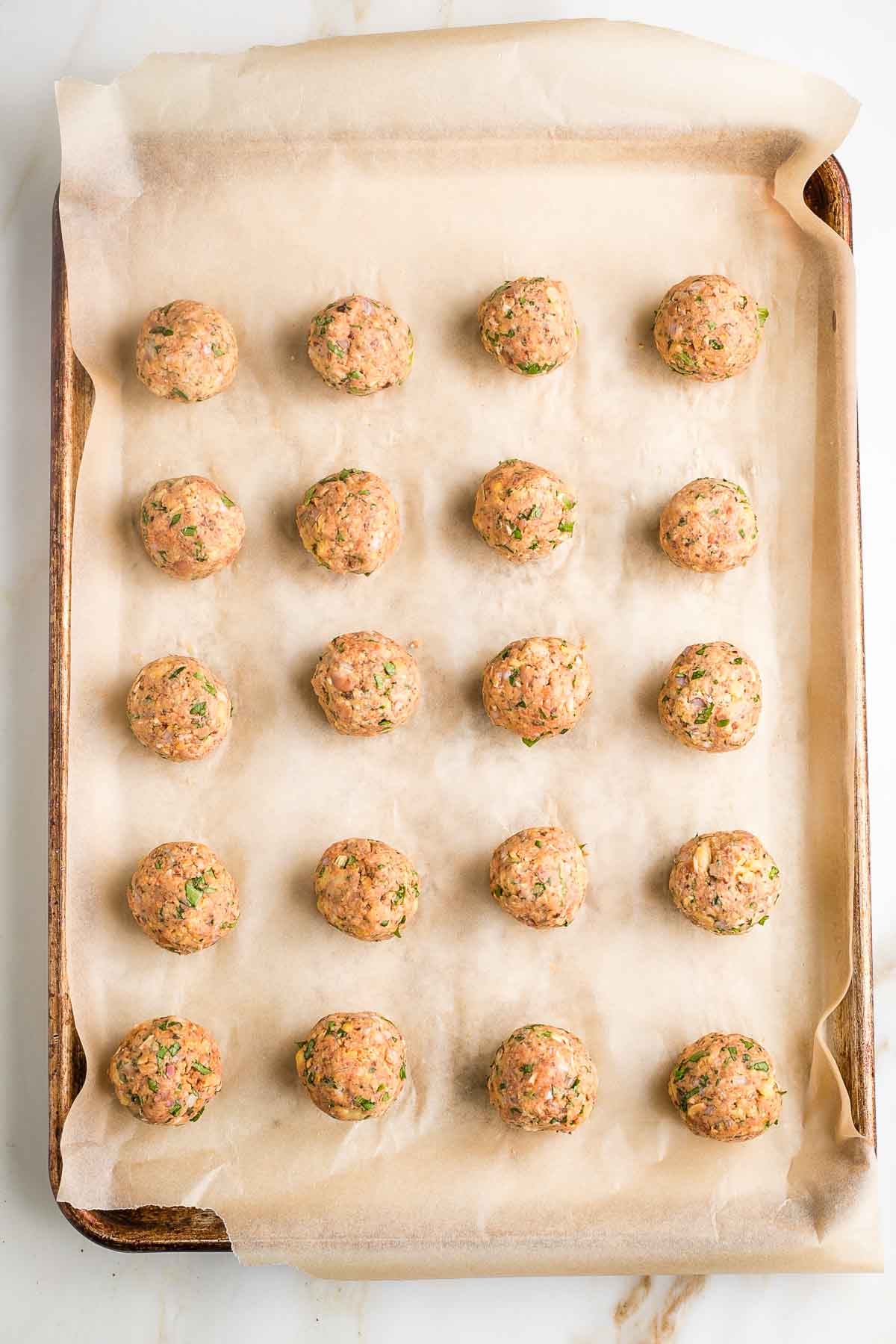 Veggie meatballs rolled into balls on a large baking tray with parchment paper.