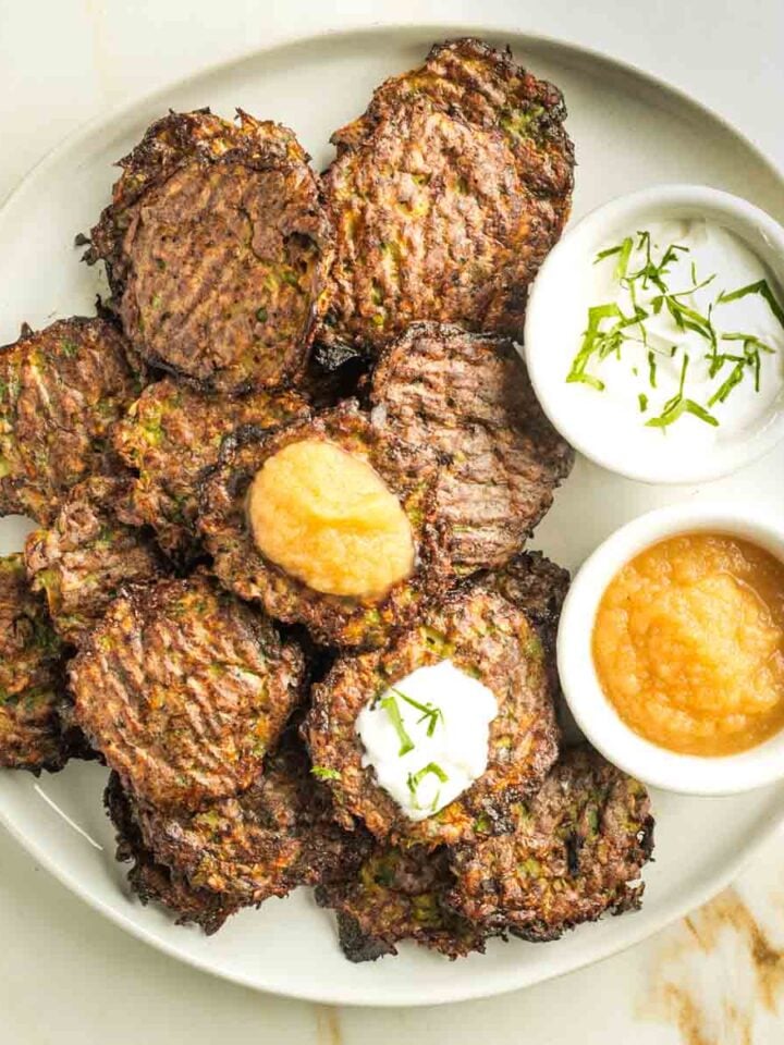 Crispy baked Brussels sprouts latkes topped with applesauce and dairy-free sour cream, with dipping bowls on the side.