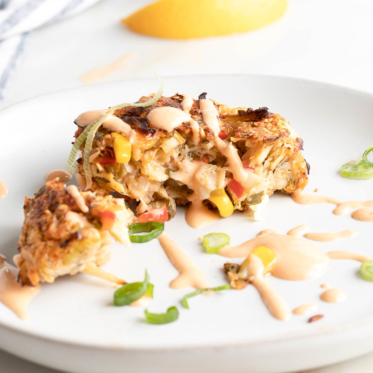 Vegan crab cake cut open to show texture, plus some drizzled sriracha sauce dripping down.