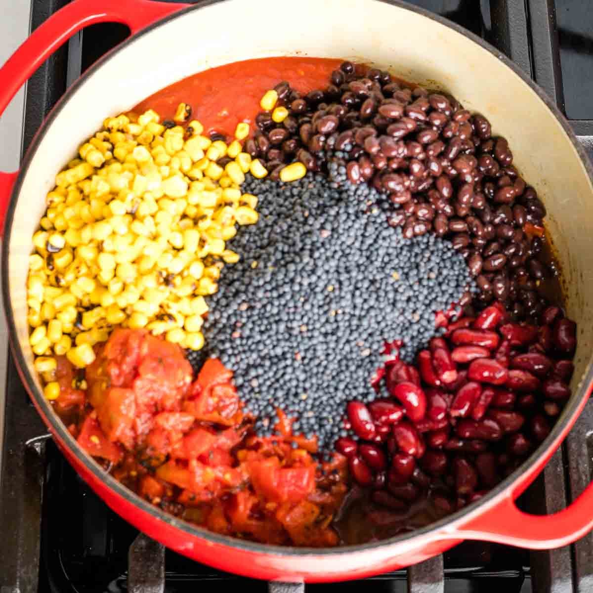 Dutch oven with chili ingredients. Visible is canned diced tomatoes, black beans, kidney beans, frozen corn and dried black beluga lentils.