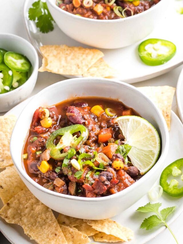 Bowl of chunky chili with jalapeno slices and a wedge of lime.