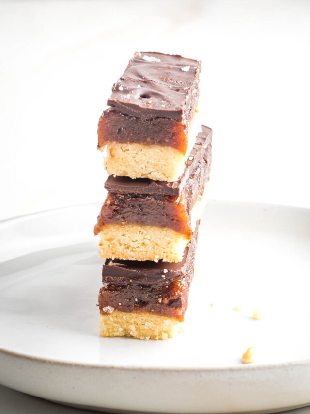 Three homemade twix bars stacked on top of each other. You can see the three layers: cookie, caramel and chocolate on the side.
