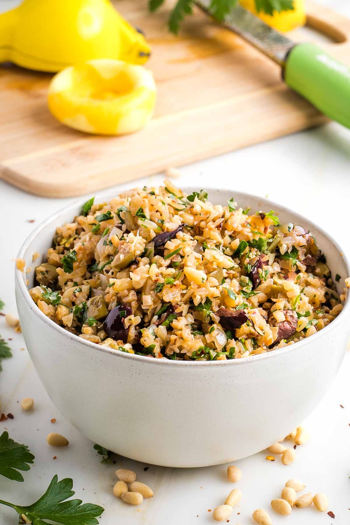 Cauliflower Rice with olives, pine nuts and fresh parsley, with lemon in the background.
