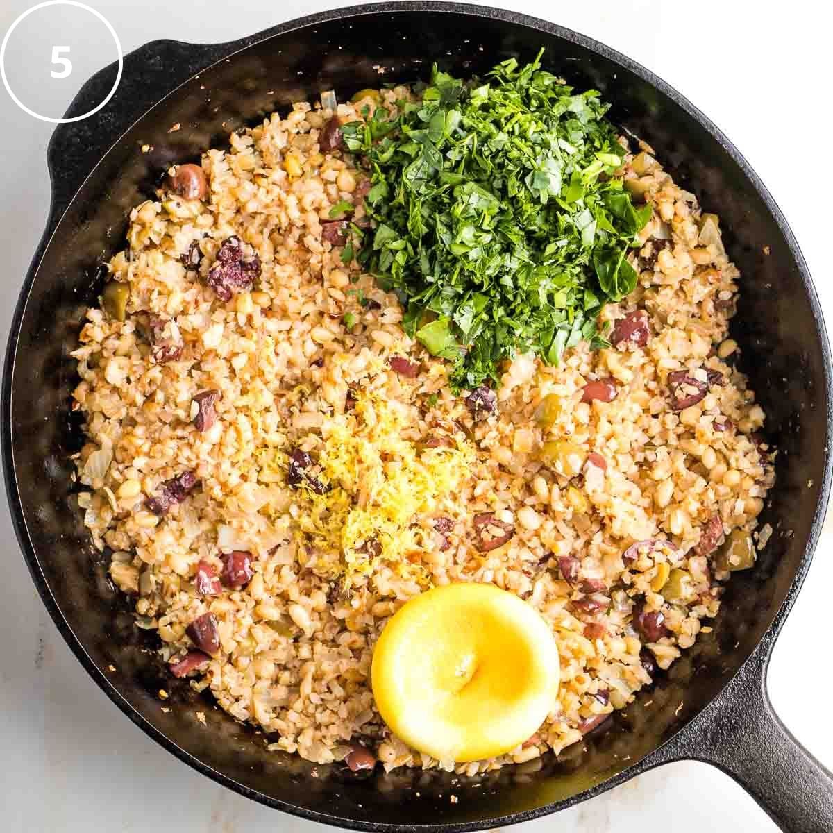 Cast iron skillet with sauteed onions, riced cauliflower and olives, plus a lemon and a handful of parsley.