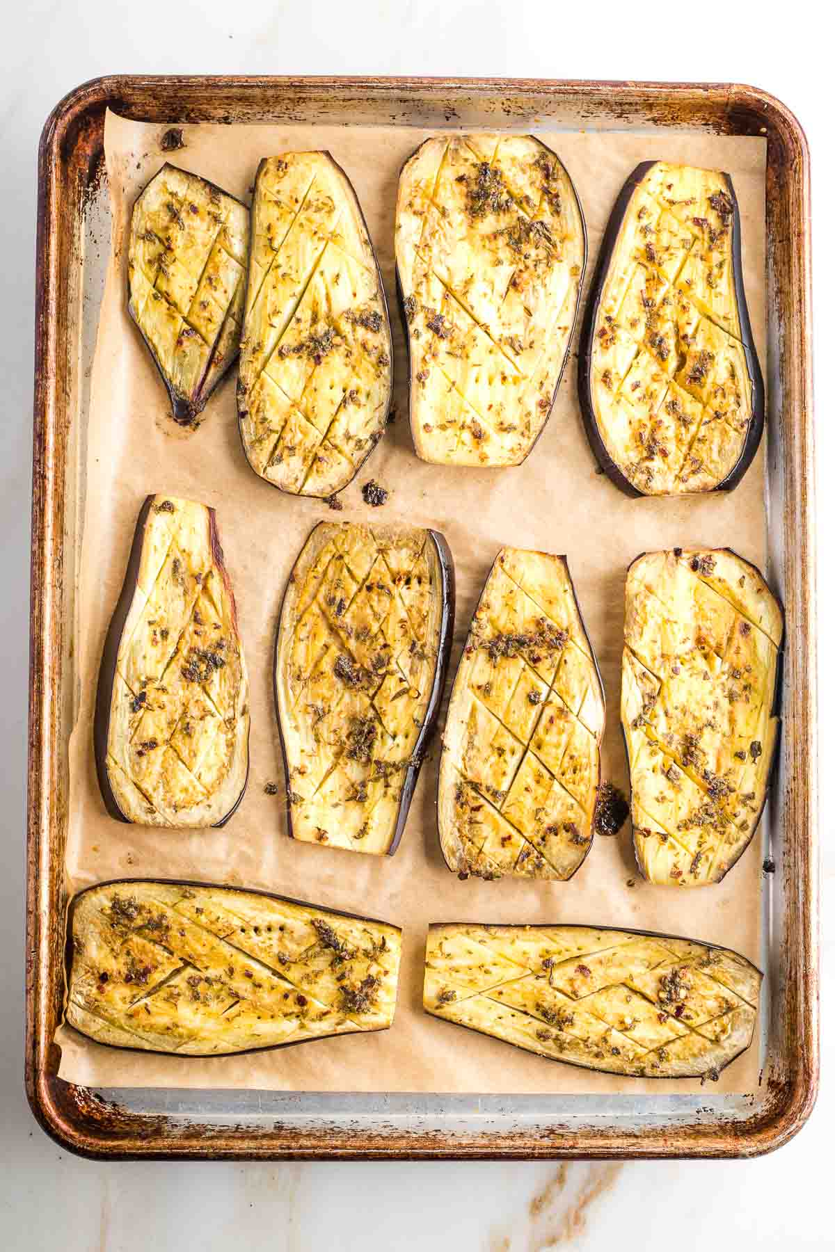 Slices of eggplant brushed with a marinade on a parchment lined sheet pan. 