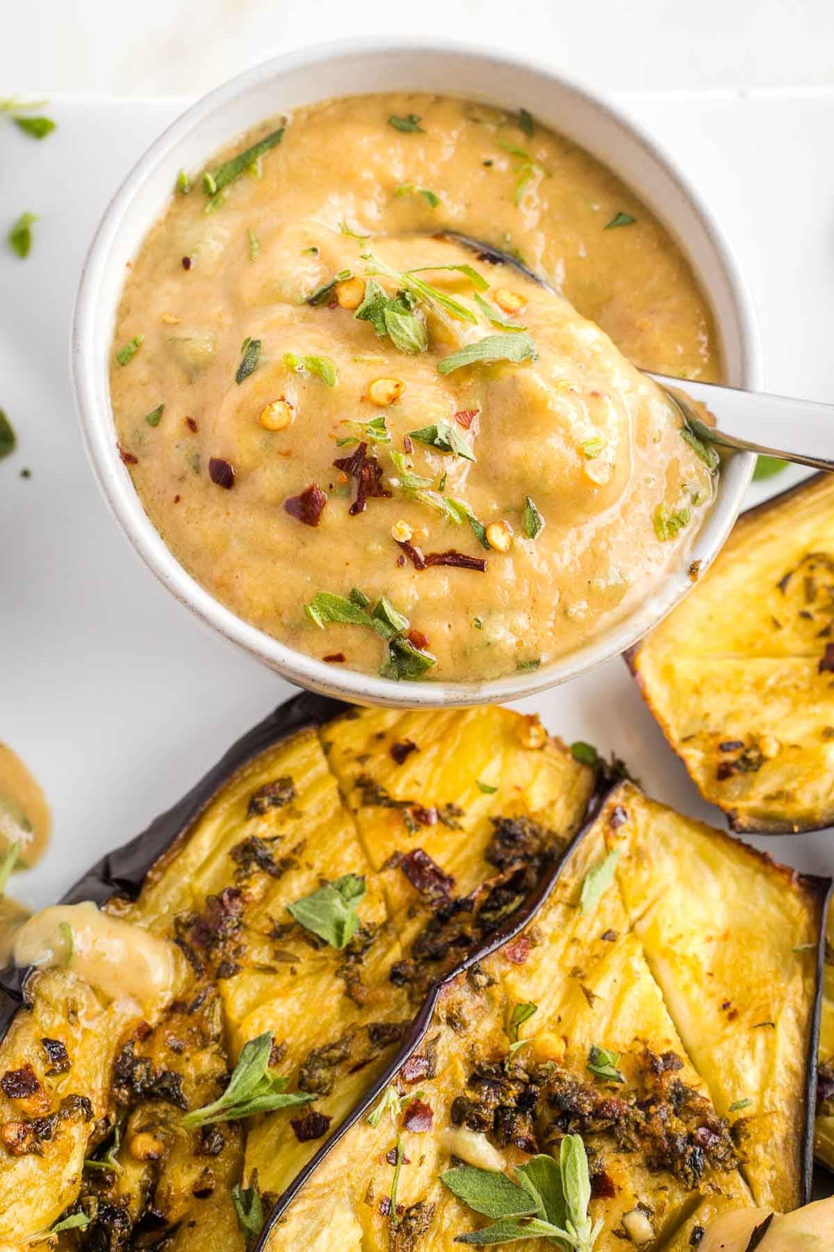Scooping and herbed tahini sauce onto eggplant slices that have been cooked in a mediterranean marinade. 