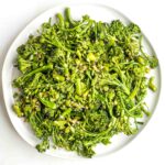 Plate filled with cooked baby broccoli with pieces of garlic.
