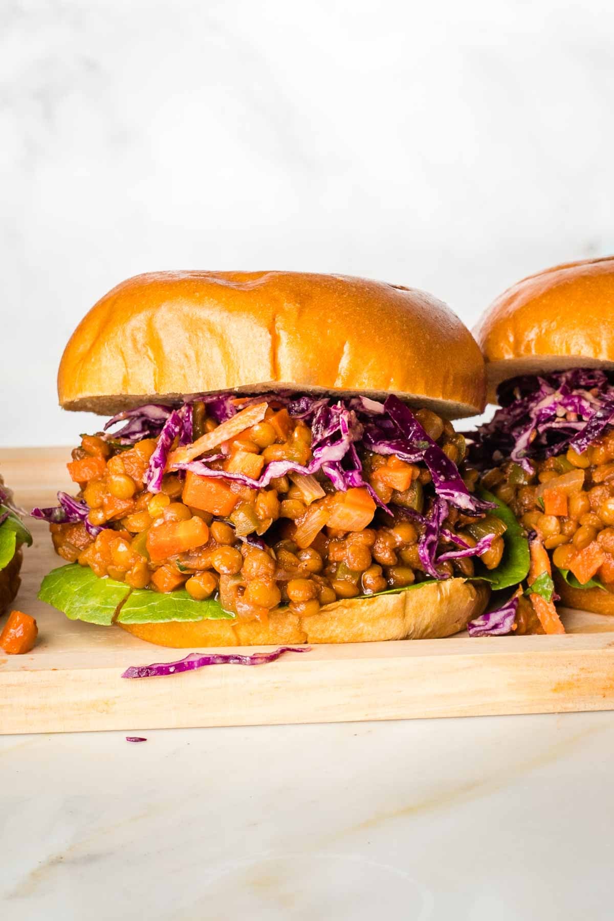 Head on shot of a vegan sloppy joe sandwich with tomato sauce, purple cabbage and a piece of green lettuce.