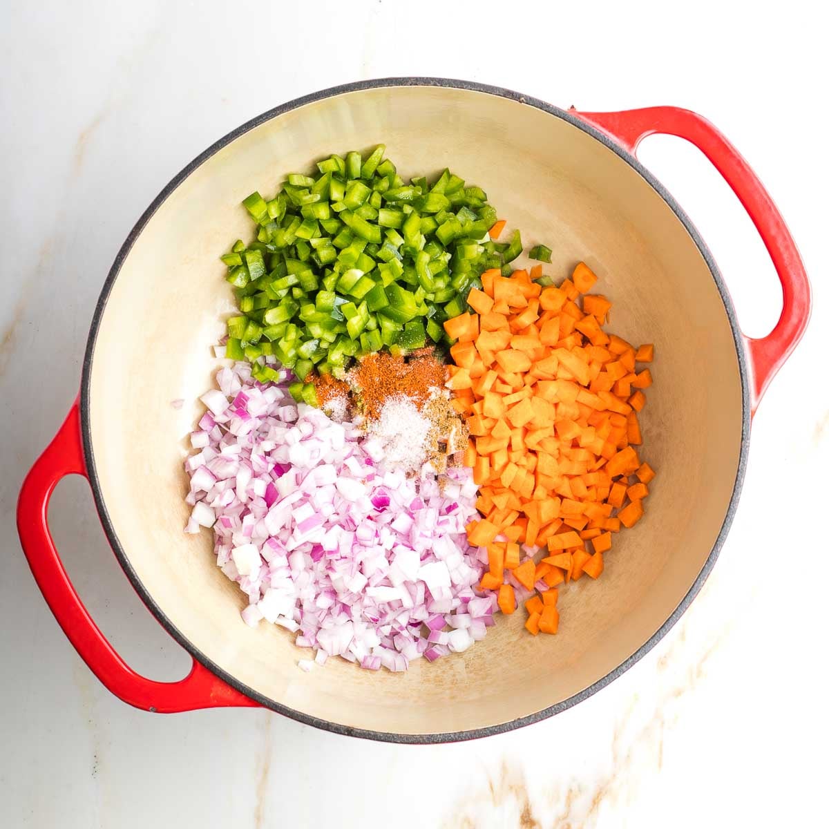 Dutch oven with sections of chopped onion, carrot and green pepper.