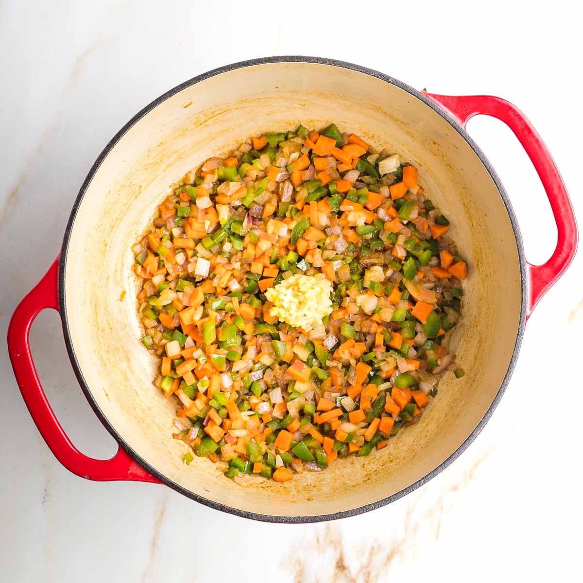 Dutch oven with diced carrots, onions, peppers plus grated garlic on top. 