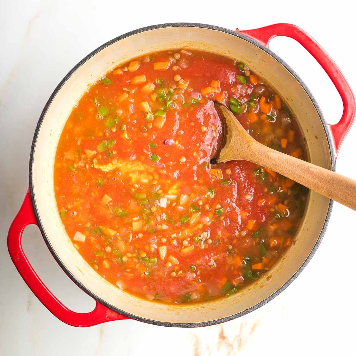 Veggies and lentils in a red tomato sauce, stirred with wooden spoon.