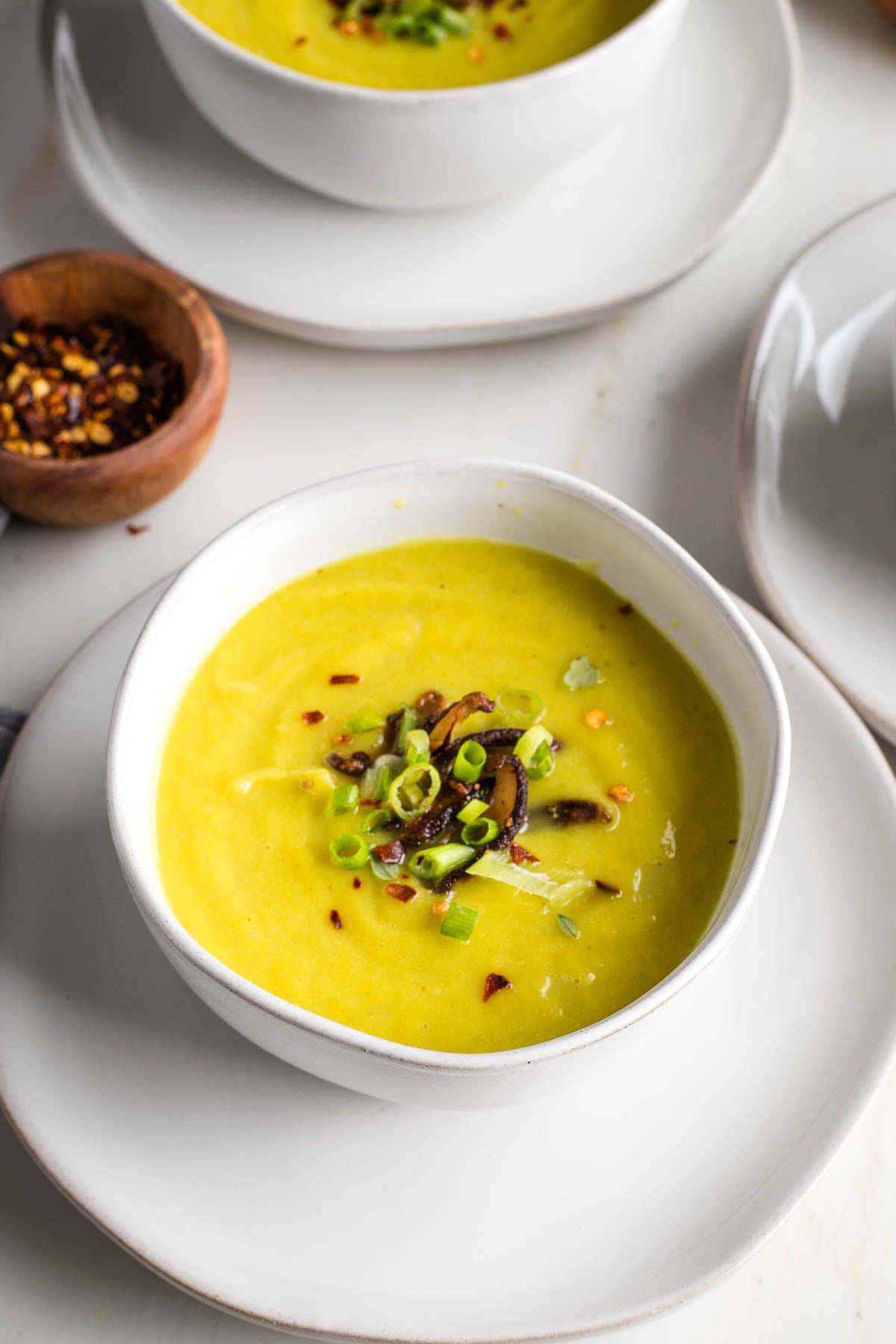 Bowl of leek soup, garnished with sauteed mushrooms, sliced scallions and red pepper.