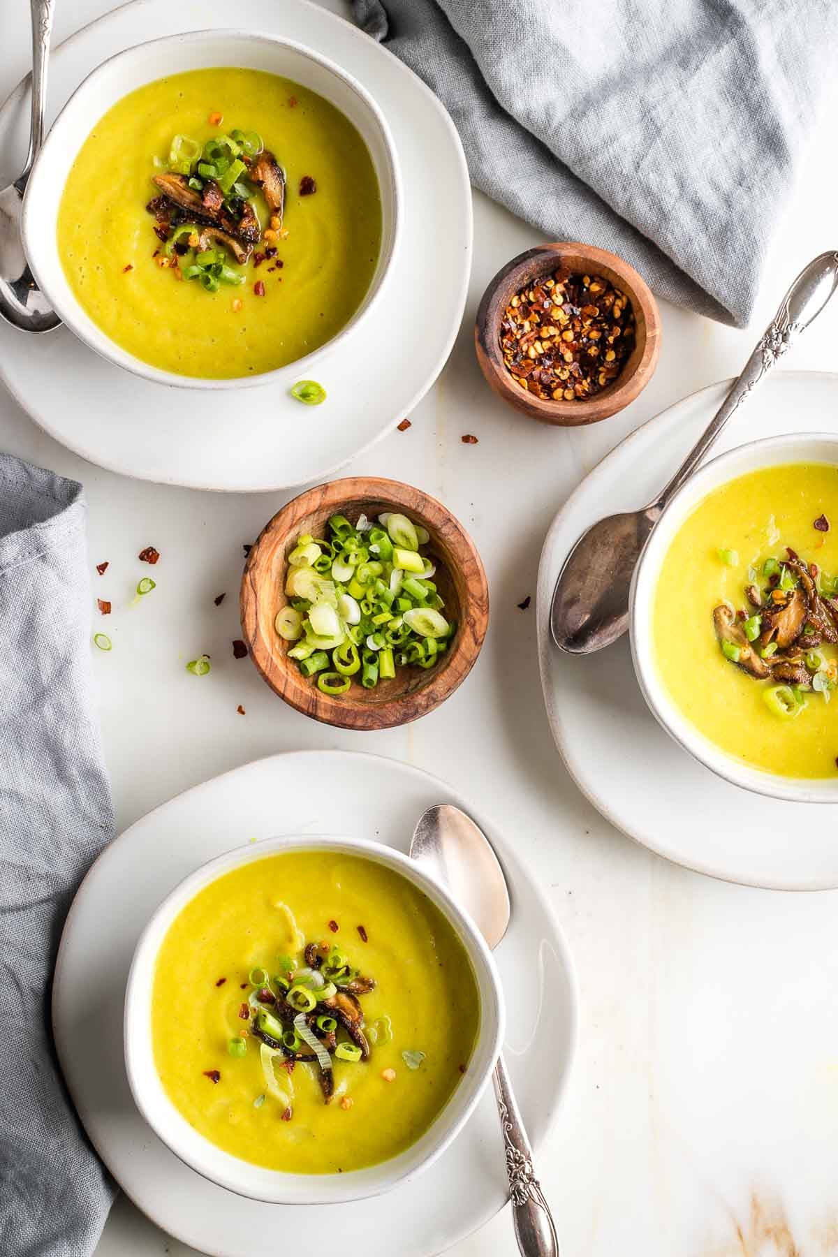 Three bowls of yellowish green pureed soup with sauteed mushrooms and scallions on top.