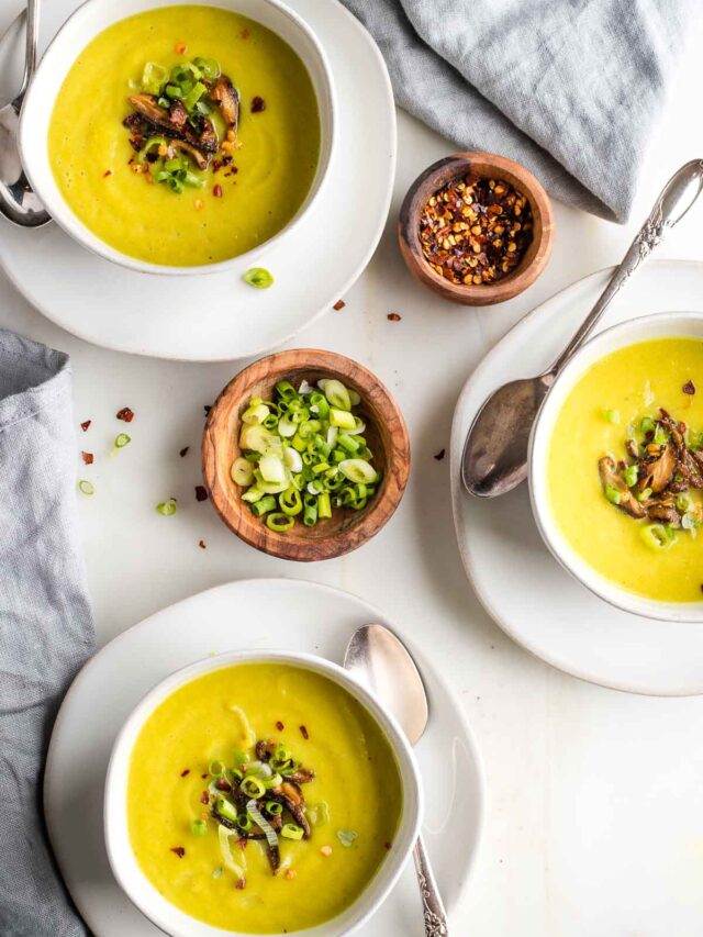 Three bowls of yellowish green pureed soup with sauteed mushrooms and scallions on top.