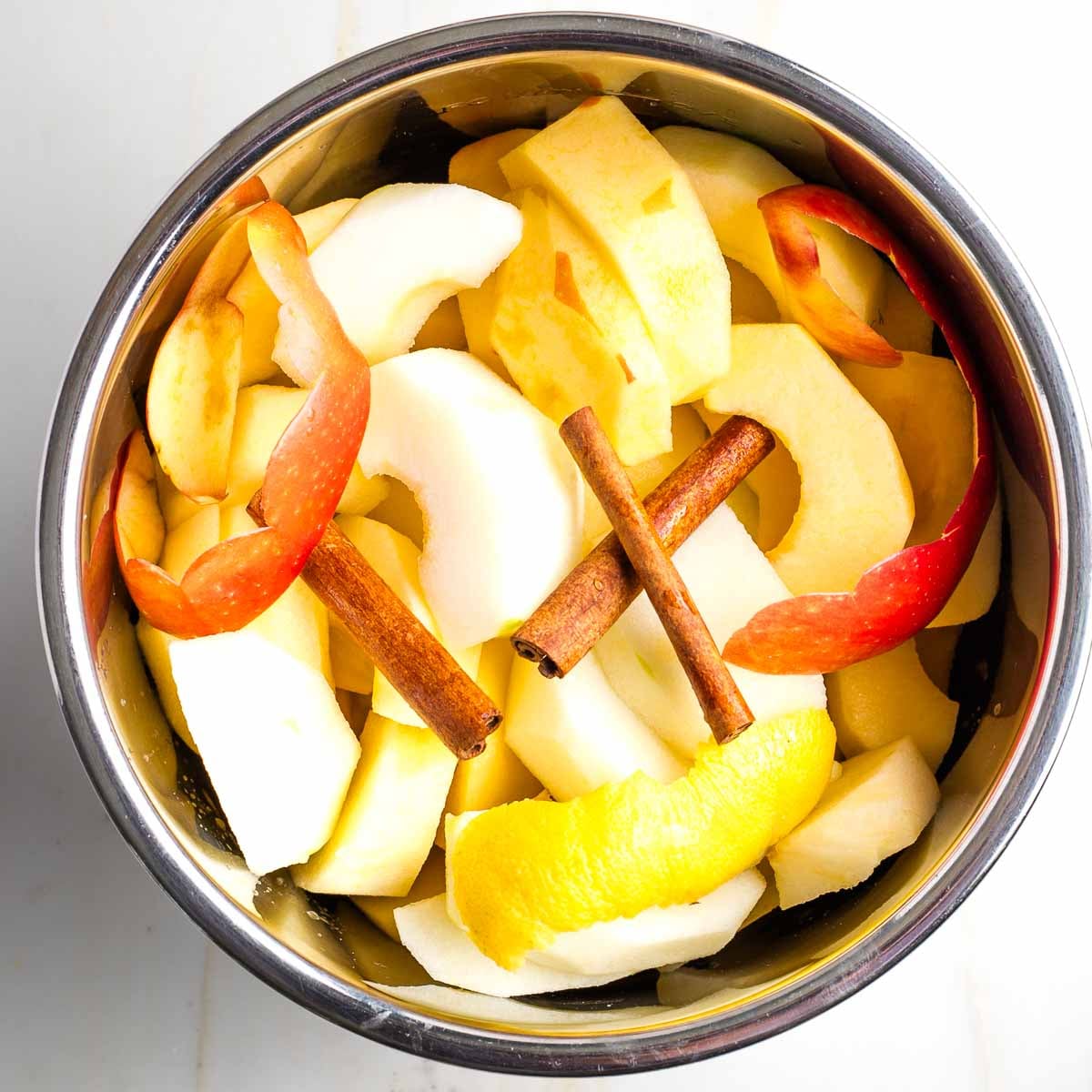 Apple chunks, lemon peel and cinnamon sticks in the bowl of an instant pot.