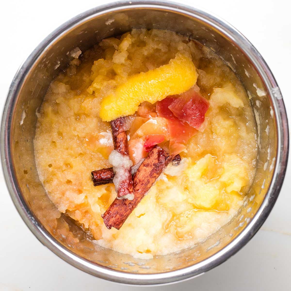 Instant pot with cooked applesauce, cinnamon sticks, apple peel and lemon rind.