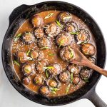 Cast iron skillet filled with saucy mushrooms, sprinkled with scallions and sesame seeds.