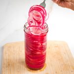 A forkful of pickled red onions coming out of a jar of more.