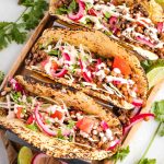 Bright colorful tacos filled with lentils, pickled onions, cabbage, tomatoes and drizzled with hot sauce.