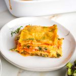 Layers of noodles, greens, zucchini, bechamel and marinara shown on a side view of a piece of lasagna.