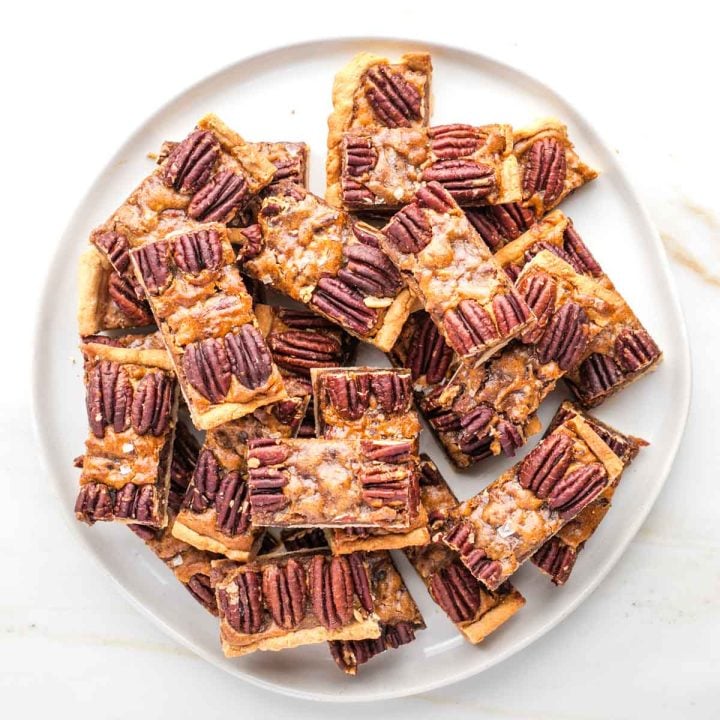Plate piled with pecan pie bars, with a pie crust, caramel layer and pecan halves decorating the top.