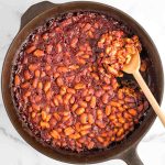 Baked beans in a cast iron skillet with wooden spoon.