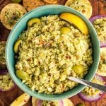 Bowl of green olive tapenade with capers and lemon, surrounded by crackers and radish slices with the olive spread.
