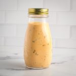 Bottle of burger sauce that's orangish with bits of pickles showing.