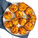 Individual sweet potato kugel cups on a plate, sprinkled with fresh herbs.