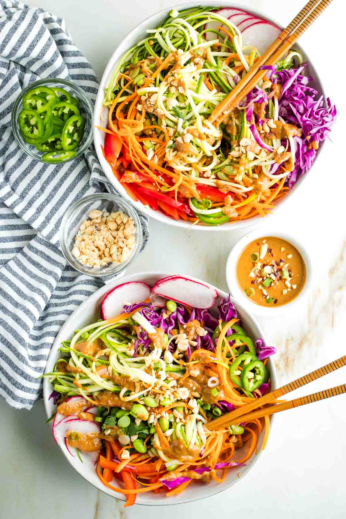 Noodles made from zucchini and carrots, twirled onto chopsticks, covered in peanut sauce with more colorful veggies in the bowl, sprinkled with peanuts and jalapenos.