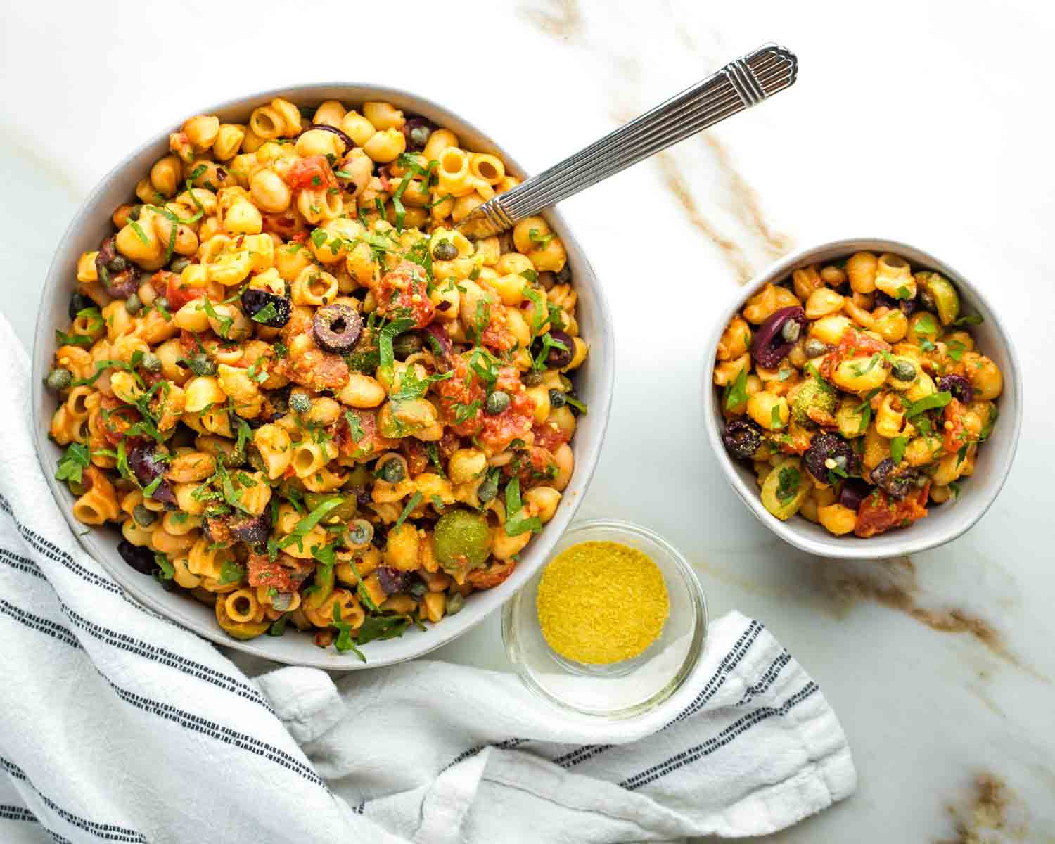 Small and large bowl of vegan pasta puttanesca with white beans. 