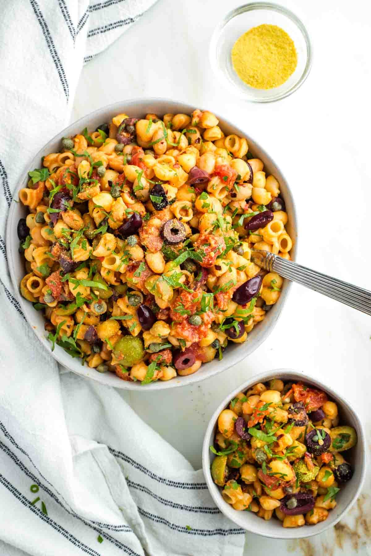 One large and one small bowl of puttanesca pasta with white beans, olives and capers.