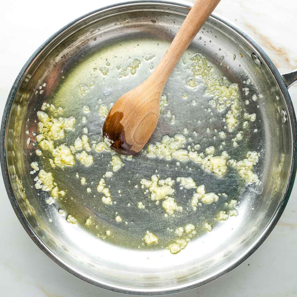 Crushed garlic in olive oil, pushed around by a wooden spoon in a skillet.
