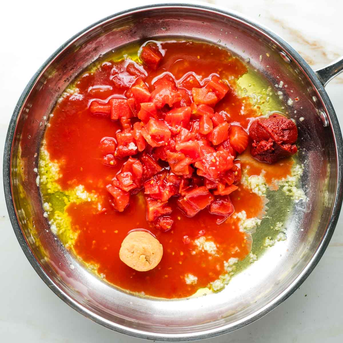 Diced tomatoes, tomato paste and miso paste in a skillet with garlic and olive oil.