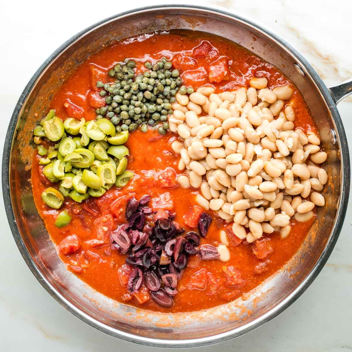 Saucy diced tomatoes with chopped olives, capers and white beans in a skillet.