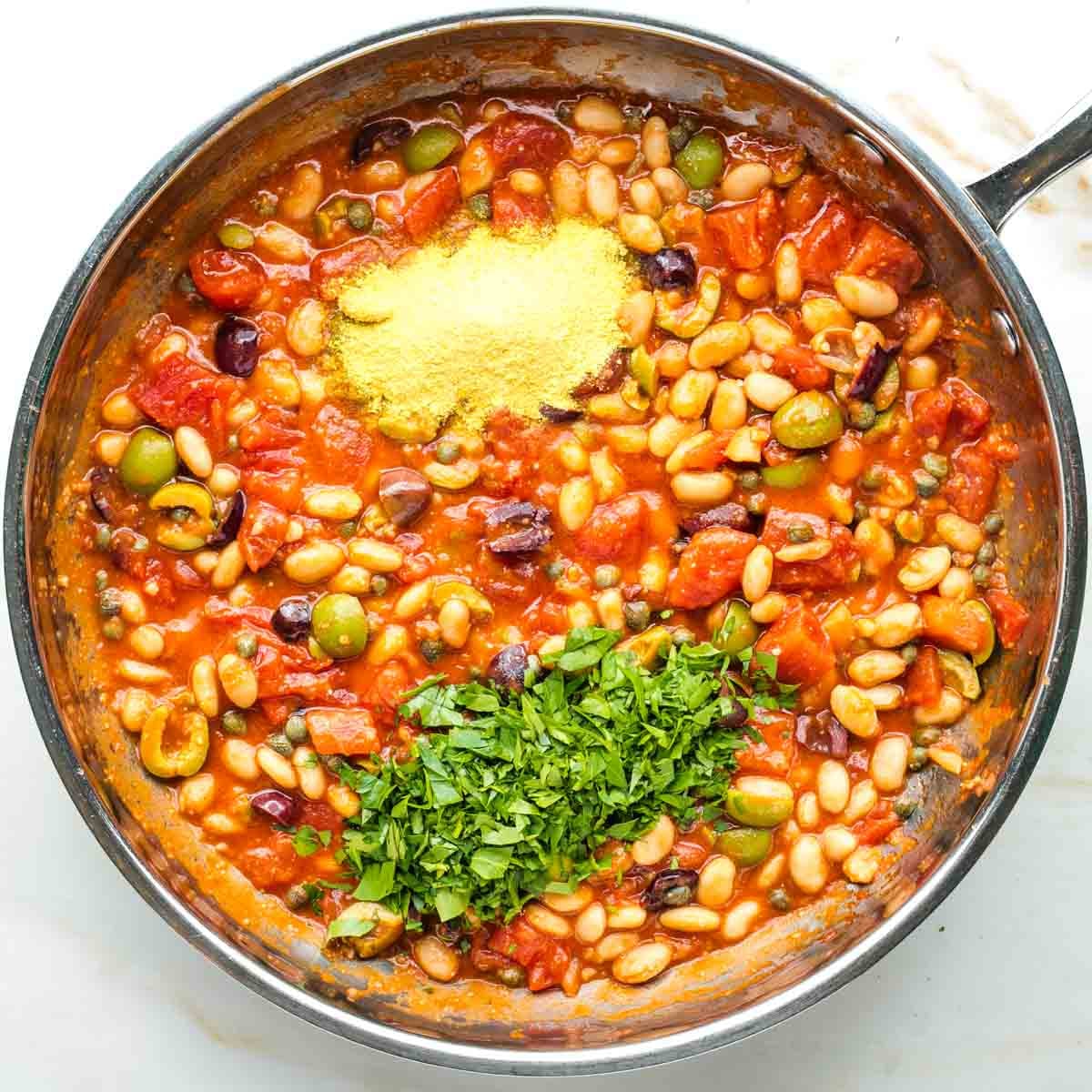 Nutritional yeast and fresh chopped parsley on top of a chunky puttanesca sauce with white beans.