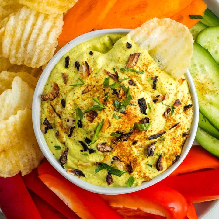 Zucchini and onion dip sprinkled with crispy onions, parsley and paprika. Surrounded by colorful veggies and chips.