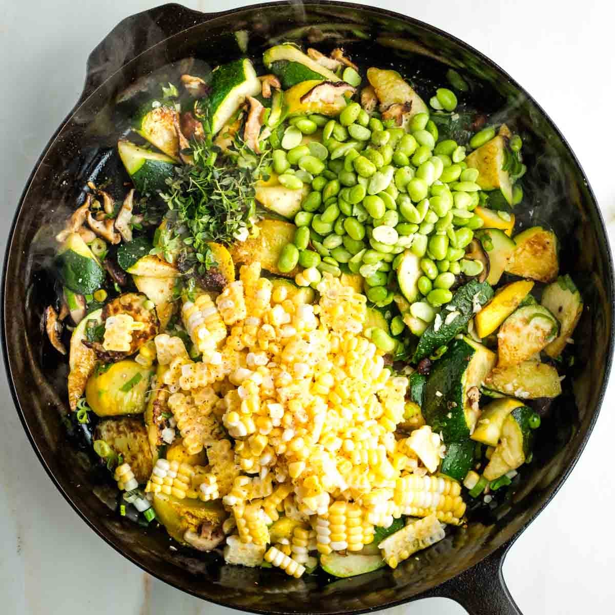 Corn kernels, edamame beans and fresh thyme on top of charred zucchini and mushrooms in a skillet.