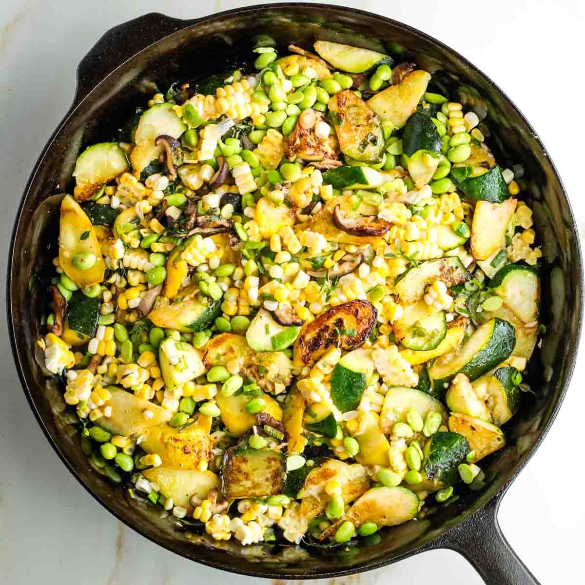 Zucchini, corn, edamame, mushrooms and scallions cooking in a cast iron skillet.