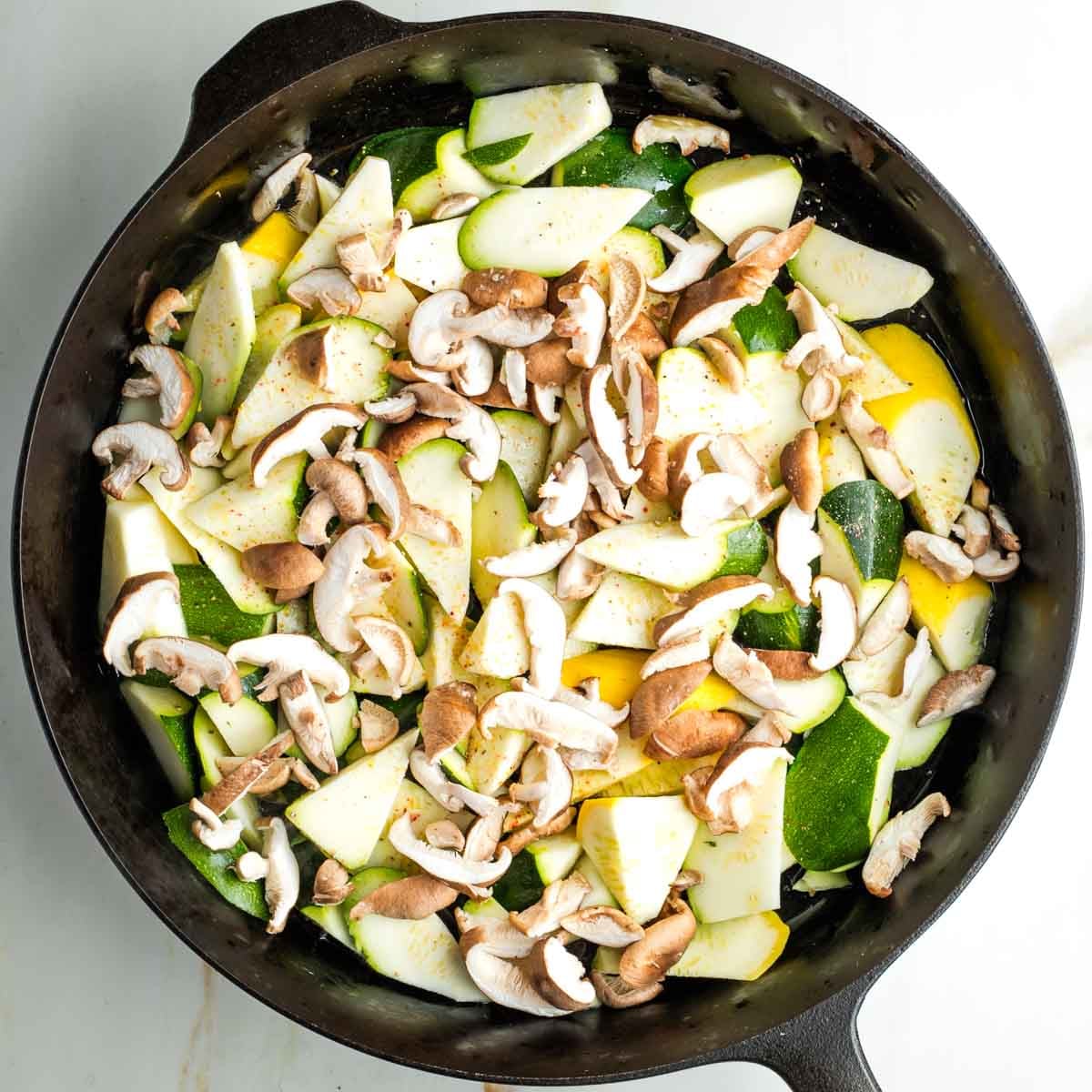 Raw zucchini and yellow summer squash in a skillet with sliced shiitake mushrooms sprinkled with salt and pepper.