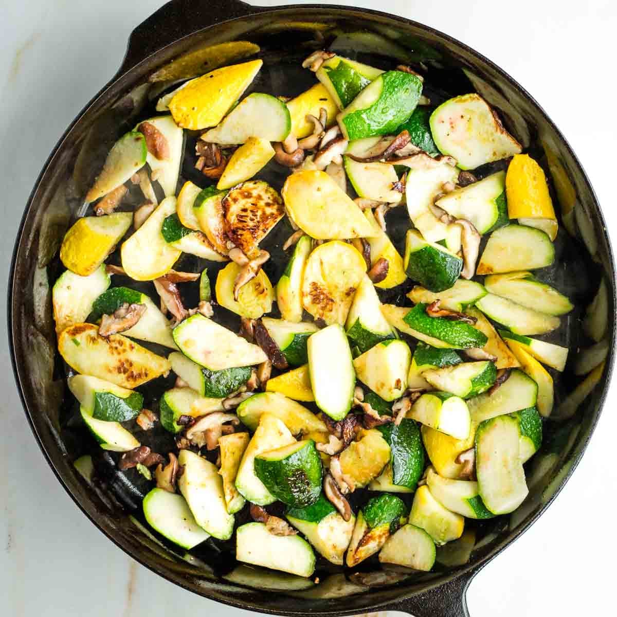 Chunks of zucchini and summer squash with mushrooms, charred in a skillet.