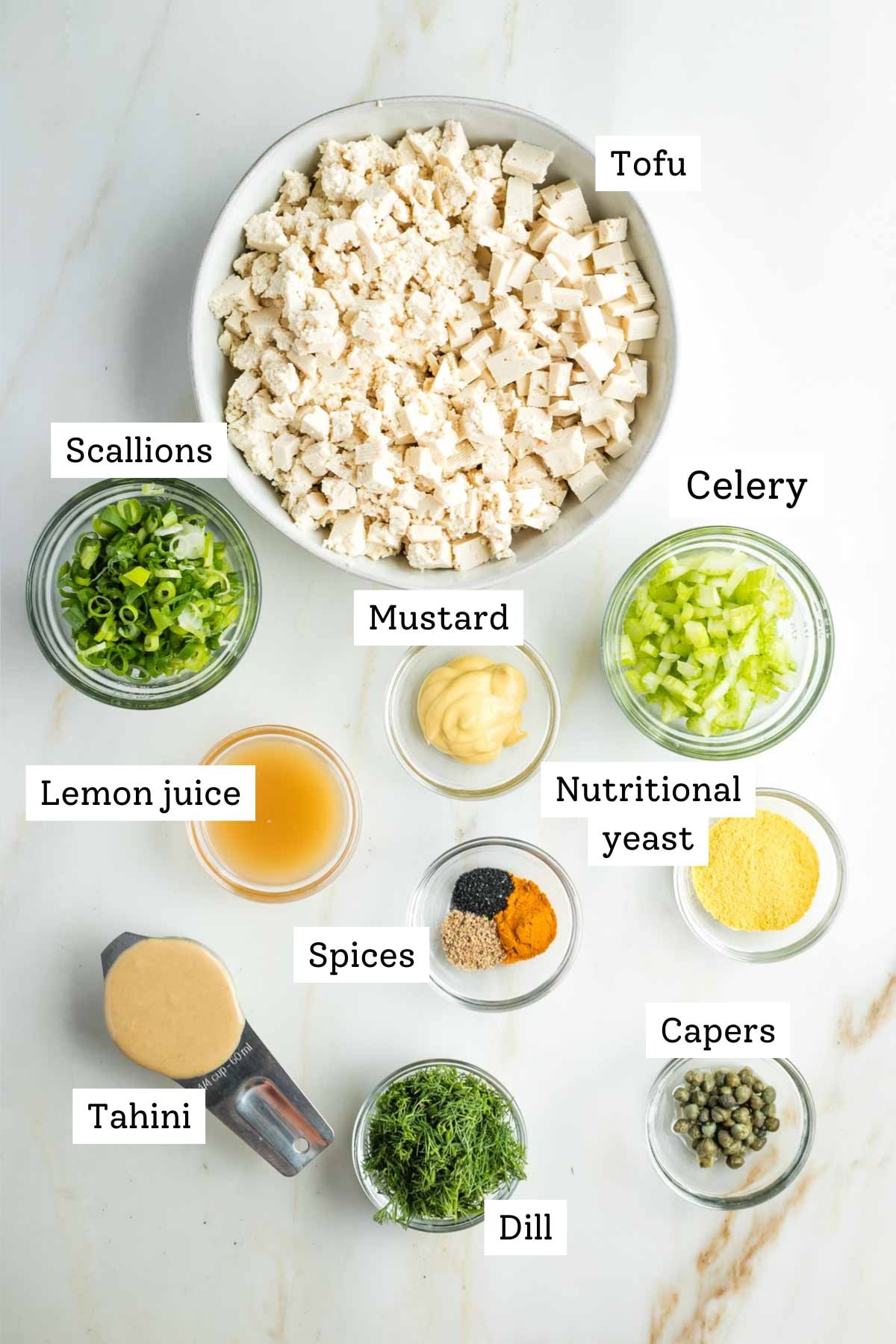 Labeled ingredients for vegan egg salad: tofu, scallions, mustard, lemon juice, tahini, spices, capers, celery. nutritional yeast.