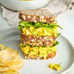 Tofu egg salad on sourdough, stacked with green lettuce in between and chips on the side.