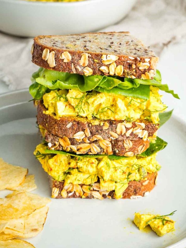 Tofu egg salad on sourdough, stacked with green lettuce in between and chips on the side.