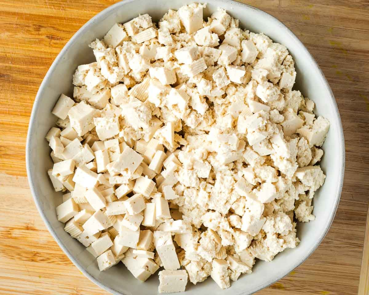 Bowl of tofu, half roughly torn into small pieces and the other half cut into neat little cubes.