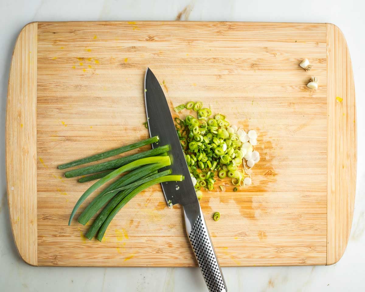 Thinly slicing white and green parts of scallions.